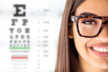 Close up of young woman wearing eyeglasses with eyechart in the background. Eyewear. Closeup view of young woman and blurred eye chart on background. Space for text - obrazy, fototapety, plakaty