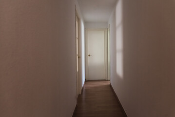 Scary light-walled hallway with a closed door illuminated by the dim shadow of a window, copy space.