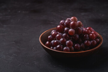 Fresh ripe grape berries in brown wooden bowl on dark stone background, angle view