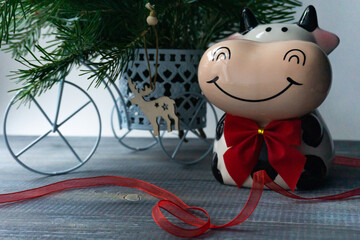 Funny cow symbol of 2021. Funny cow with a red bow on the background of a Christmas tree. Copyspace. 