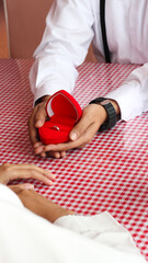 The man holding the red box in the shape of love is proposing to his girlfriend.