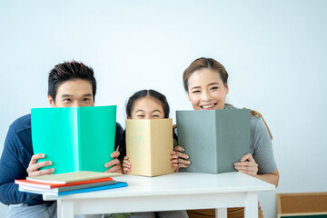 Adorable attractive beautiful asian family, Asian young mother and father with little daughter sit at desk and holding book with funny. Education concept.