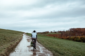 Man, visible from behind, on a bicycle cycling uphill in an amazing autumn scenery. Very colourful foliage and cloudy but blue sky.