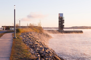 The Samuel-De Champlain walk along the St. Lawrence River leading to a tall observation tower and pavilion seen through sea smoke during a morning golden hour, Quebec City, Quebec, Canada © Anne Richard
