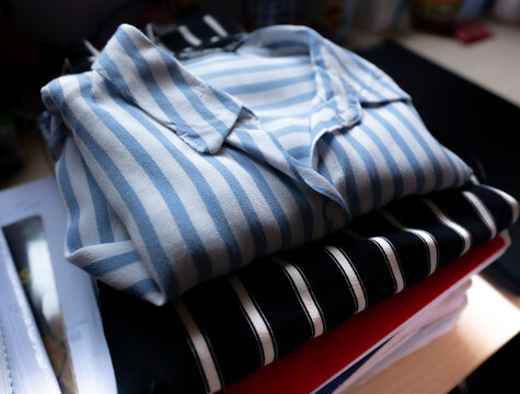Clothes, teenage winter folded shirts, student in his bedroom with books underneath, natural lighting from the window.