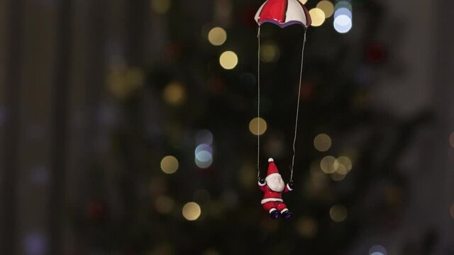 A toy Santa Claus slowly descends by parachute under the Christmas tree. Christmas tale