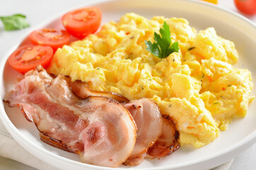 Scrambled eggs, fried bacon and tomatoes on white plate