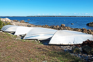 A row of four dinghies or rowing boats are pulled up on a beach in Fairhaven, Massachusetts.