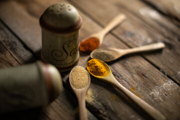 Top view of colorful spices in wooden spoon lying on a old wooden table in a dark kitchen. Lot of copy space. Chili, pepper, garlic, curcuma and salt in small pots. Shallow depth of field