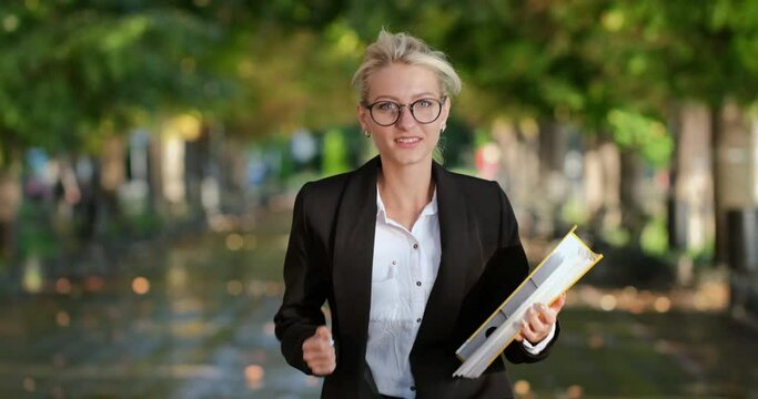 A girl with a yellow documents folder runs on the spot along the road in the city, with an insistent expression on her face. An attempt to catch up with lost time. 