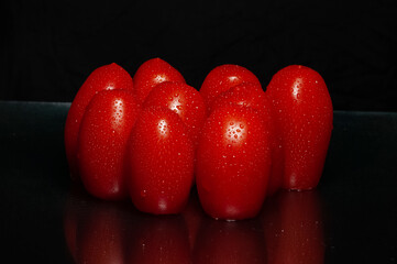 Close-up on wet cherry tomatoes. Drops of water and bright shiny red. black background with space for text