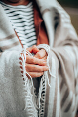 Women's hands in a warm knitted blanket to keep warm in cold October weather in the forest or park