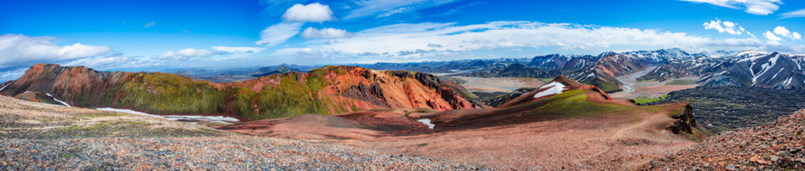 Panoramic amazing Icelandic landscape of colorful rainbow volcanic Landmannalaugar mountains, volcanic craters at famous Laugavegur hiking trail with rare blue sky, and red volcano soil in Iceland.