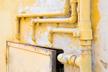 Old domestic protective metal box of water and methane gas against a damaged varnished plaster wall with metal pipeline fixed with brackets on it
