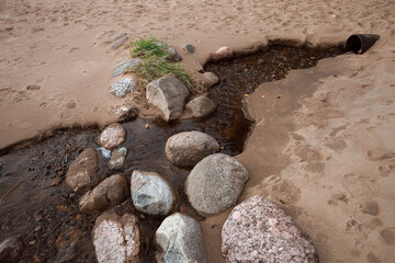 A sewage pipe overlooking the beach, which washed out the coast to form a stream with brown water. Close-up.