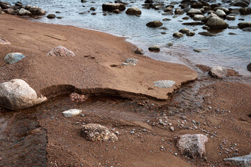 Sandy shore washed out by a stream. Blue sky reflected in smooth water. Autumn mood