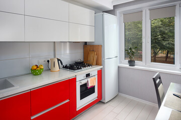 Upscale Maple Red and Smoky White kitchen in luxury home with stoneware countertop flat wooden panels design with window stove fridge and dining table.