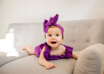 a little girl in a purple suit is lying on a gray sofa and smiling