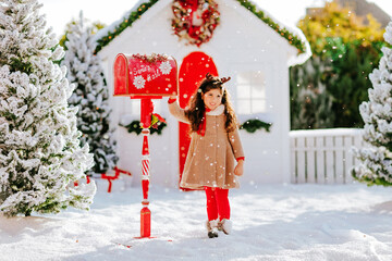 A beautiful girl sends a letter to Santa in a red mailbox 