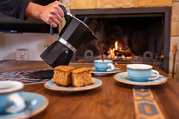 Fototapeta na wymiar Coffee cups with coffee pot and lit fireplace