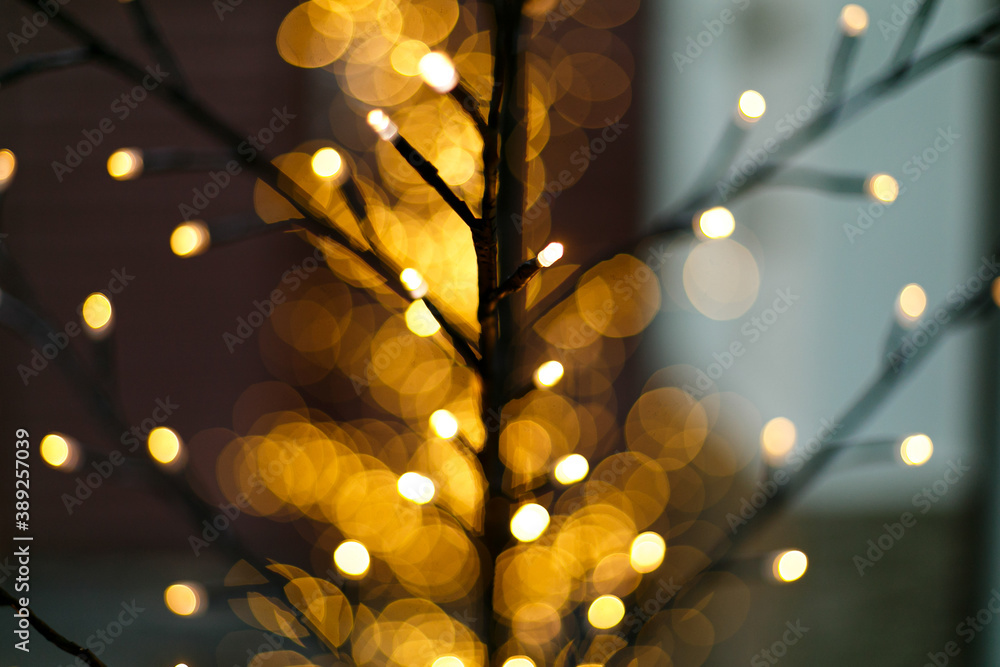 Wall mural Stylish illuminated tree with warm golden lights bokeh, festive decor in evening. Winter holiday