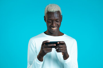 Handsome african man playing game on smartphone on blue studio wall. Using modern technology - apps, social networks.