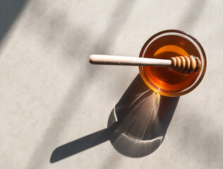 Wooden honey dipper in honey on off-white background in natural sunlight.fresh honey in glass bowl with wooden honey stick.