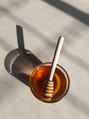 Wooden honey dipper in honey on off-white background in natural sunlight.fresh honey in glass bowl...