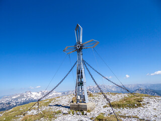 Fototapeta na wymiar A cross on the top of Hochturm, Austrian Alps. The cross is supported by 4 metal ropes. Dense forest on both sides. Alpine landscape on a sunny, summery day. Exploring the nature
