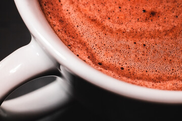 Fotografía macro de una taza blanca llena de café con espuma cremosa tipo capuccino