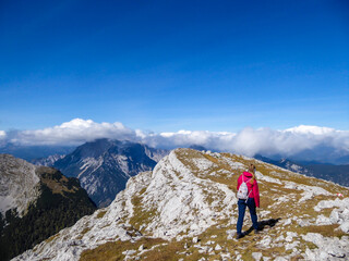 Fototapeta premium A woman in pink jacket enjoying the Alpine landscape from Hochzin?dl peak in Austria. Steep, sharp mountains around her. Fall landscape - golden grass. Exploring and experiencing the nature