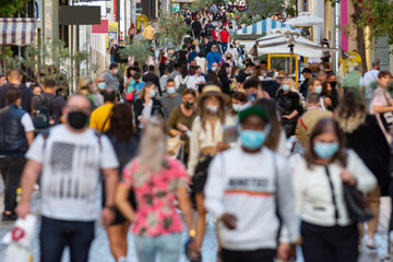 crowd goes up and down a busy shopping street wearing a protective mask