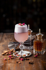 Pink alcoholic cocktail with foam, decorated with dry roses. drink on wooden background. bartender attributes are next to each other.