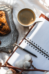 Coffee mug with croissant and empty notebook and pencil for business plan and design ideas onon white cloth from above, cozy and tasty breakfast, vintage toned