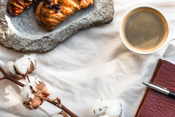 Coffee mug with croissant and empty notebook and pencil for business plan and design ideas onon white cloth from above, cozy and tasty breakfast, vintage toned