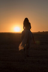 Attractive young Caucasian female with a beautiful dress riding a horse in countryside at sunset