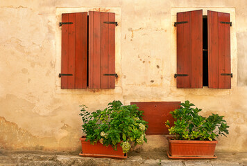 The facade of an old provincial house with two windows, closed by wooden shutters. Garden flowers...