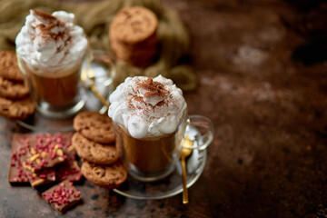 Two tall glasses with hot chocolate, whipped cream and cinnamon powder on top
