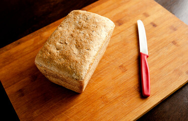 Homemade bread in the shape of a brick on a cutting board with a red knife