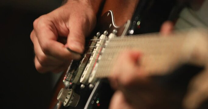 Musician playing solo using electric guitar during recording session, close up at hand and fret-board and focus on right hand in background