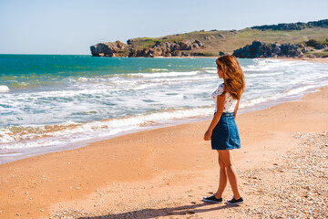 Fototapeta na wymiar Beautiful young woman with long hair walks along the Black sea on the beach
