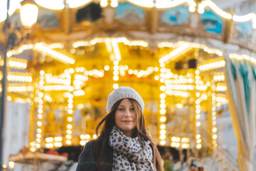 Girl visiting Europe 2020 city christmas lights, Golden carousel. Women smiling wearing a cap under the city christmas lights