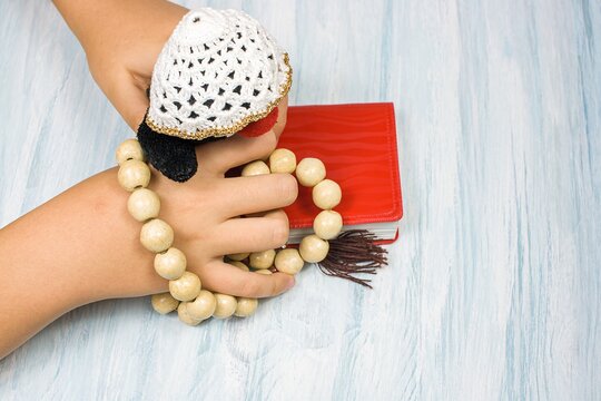 children's hands with rosary and prayer book on the table, background of religion