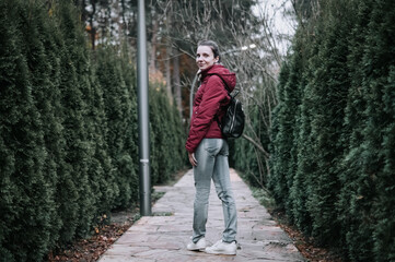 Rear view of woman walking along fir tree alley in autumn. girl with backpack walks along alley of trees