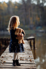 little beautiful girl holding a toy in her hands in the autumn park near the water. girl on a...