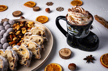Winter hot drink in funny cup, cacao with Christmas stollen on wooden board with dried fruits and nuts. Traditional german cake.Concept for postcard, holiday greeting.