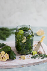 Cucumbers in a jar with garlic and dill on wood board a light background.