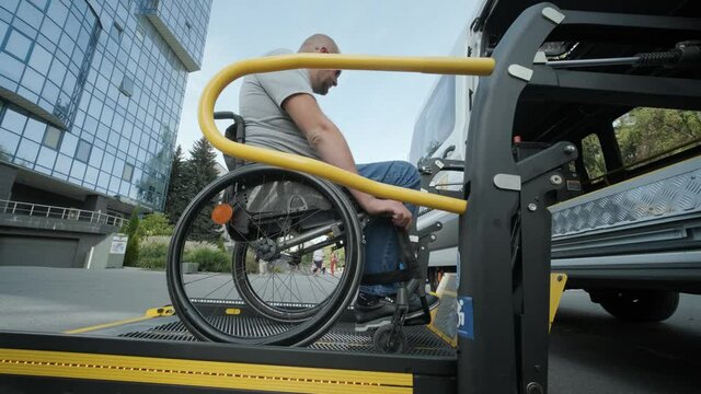 A Man In A Wheelchair On A Lift Of A Vehicle For People With Disabilities. Lifting Equipment For People With Disabilities - Man In Wheelchair Near The Vehicle