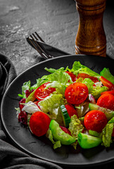 various fresh mix salad leaves with tomato, cucumber and red pepper on a black plate on Dark grey black slate background