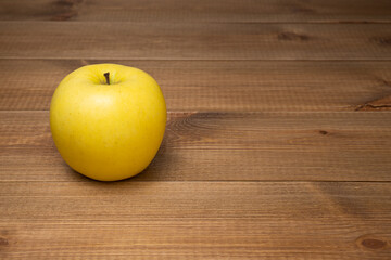 One sweet and juicy yellow golden apple on a wooden table with copy space.